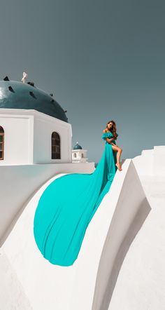 a woman in a blue dress sitting on the edge of a white building with a dome