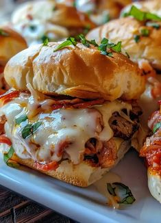 several sandwiches with meat and cheese are on a white platter next to bread rolls