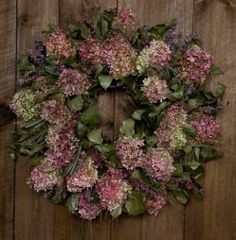 a wreath made out of pink and green flowers on a wooden fence with leaves around it