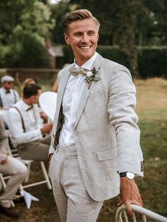 a man in a suit and bow tie standing next to other men sitting on lawn chairs