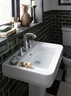 a white sink sitting next to a toilet in a bathroom under a window with pineapples on the ledge