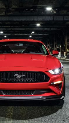 the front end of a red sports car parked in a parking lot at night with its lights on