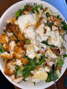 a white bowl filled with salad and dressing on top of a wooden table next to a fork