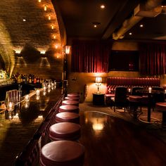 a dimly lit bar with lots of stools and lights on the wall behind it