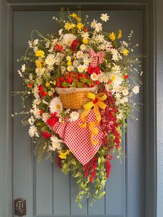 a wreath hanging on the front door decorated with flowers and a basket full of daisies