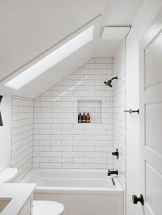 an attic bathroom with white subway tile and black faucet, toilet, sink, and bathtub