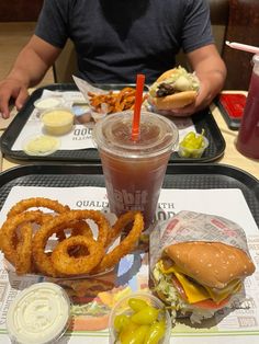 a tray topped with a sandwich and onion rings next to a drink