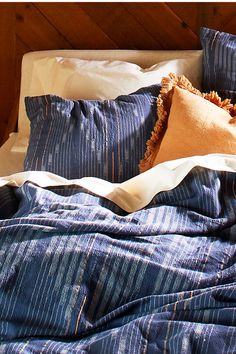 an unmade bed with blue and white striped comforter, pillows and blankets on it