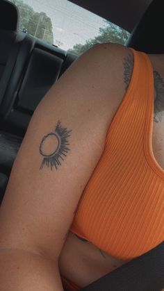 a woman in an orange top sitting in the back seat of a car with her arm tattoo