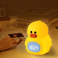 a yellow ducky alarm clock sitting on top of a table next to a book