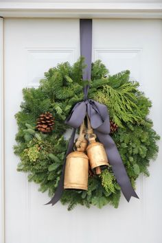 a wreath with two bells hanging from it's side and pine cones on the front door