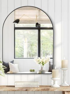 a table with flowers and candles on it in front of a large window that has a circular mirror over it