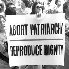 a group of people standing around each other holding up signs that read, adopt patinarchy reproduce identity