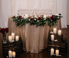 a table topped with candles and flowers next to a white chair covered in greenery