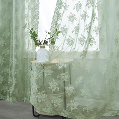 a vase with flowers sitting on a table in front of a sheered window curtain