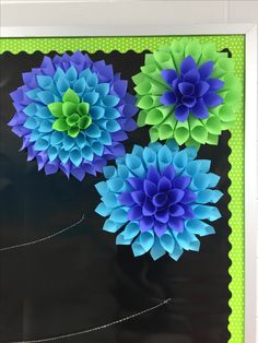 three blue and green paper flowers in a white frame on a black background with polka dots