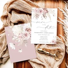 the wedding stationery is laid out on top of a wooden table with some flowers