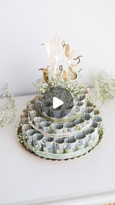 a cake made out of money sitting on top of a white table next to baby's breath flowers