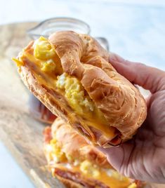 a person holding up a sandwich with eggs and cheese on it in front of a jar