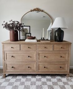 a dresser with a mirror, vases and candles on it in a living room