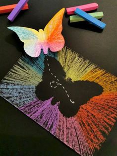 some crayons and colored pencils are on a table with a drawing of a butterfly