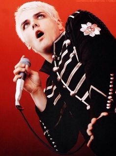 a man with white hair holding a microphone in his hand and singing into the microphone