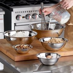 a person mixing ingredients in metal bowls on a cutting board