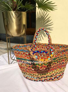 a multicolored basket sitting on top of a white table next to a potted plant