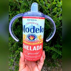 a hand holding an empty modelo bottle in front of some bushes and shrubbery