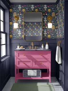 a bathroom with a pink vanity and floral wallpaper on the walls, along with a gold framed mirror