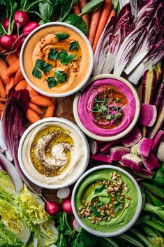 several bowls of different types of food on a wooden table with carrots, celery, lettuce and other vegetables