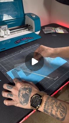 a person with tattoos is using a machine to cut out images on a piece of paper