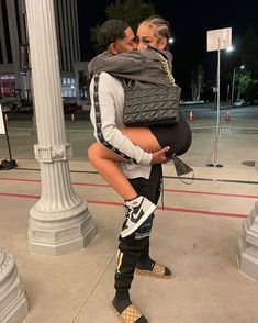 a man carrying a woman on his back while standing next to a lamp post at night