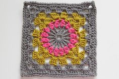 a crocheted square with a pink and yellow flower in the center on a white surface