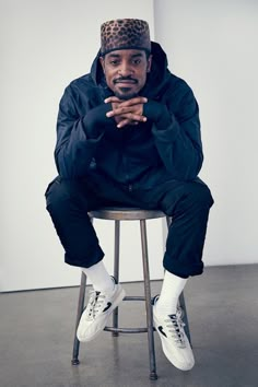 a man sitting on top of a stool wearing a leopard print hat and black jacket