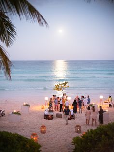 a group of people standing on top of a sandy beach next to the ocean at night