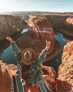 a woman sitting on top of a cliff with her arms in the air