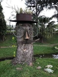 a tree trunk with a hat and glasses on it's face, sitting in the grass