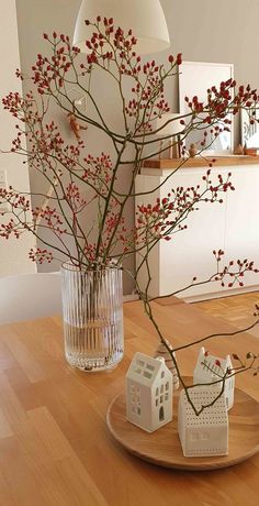 a wooden table topped with vases filled with red flowers and small white houses sitting on top of it