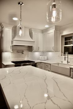 a kitchen with marble counter tops and white cabinets, lights above the stove and sink