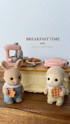 two small stuffed animals sitting next to each other on a table with breakfast time written in the background