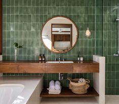 a bathroom with green tiles and a round mirror on the wall, along with a white bathtub