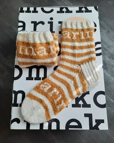 two knitted baby socks sitting on top of a white and orange sign with words