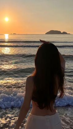 a woman standing on top of a sandy beach next to the ocean at sunset or dawn