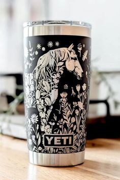 Black YETI tumbler with an intricate white floral design featuring a horse’s head among detailed wildflowers, placed on a wooden surface with a blurred background. Drawings Of Horses, Engraved Yeti Tumbler, Engraved Yeti, Yeti Tumbler, Car Restoration, Horse Drawings, Beautiful Horse, Equestrian Life, Horse Designs