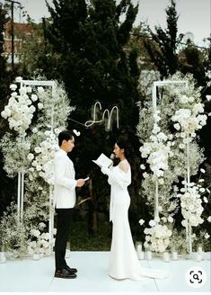 a newly married couple standing in front of an arch with white flowers and greenery