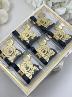 six black and gold mickey mouse napkins in a clear box with white flowers behind them