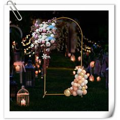 an arch decorated with balloons and flowers in front of lanterns on the grass at night