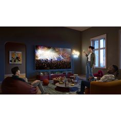 two people watching fireworks on the television screen in a living room with other people sitting and standing around