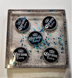 four corona extra beer bottle caps on a silver tray with blue and green confetti sprinkles